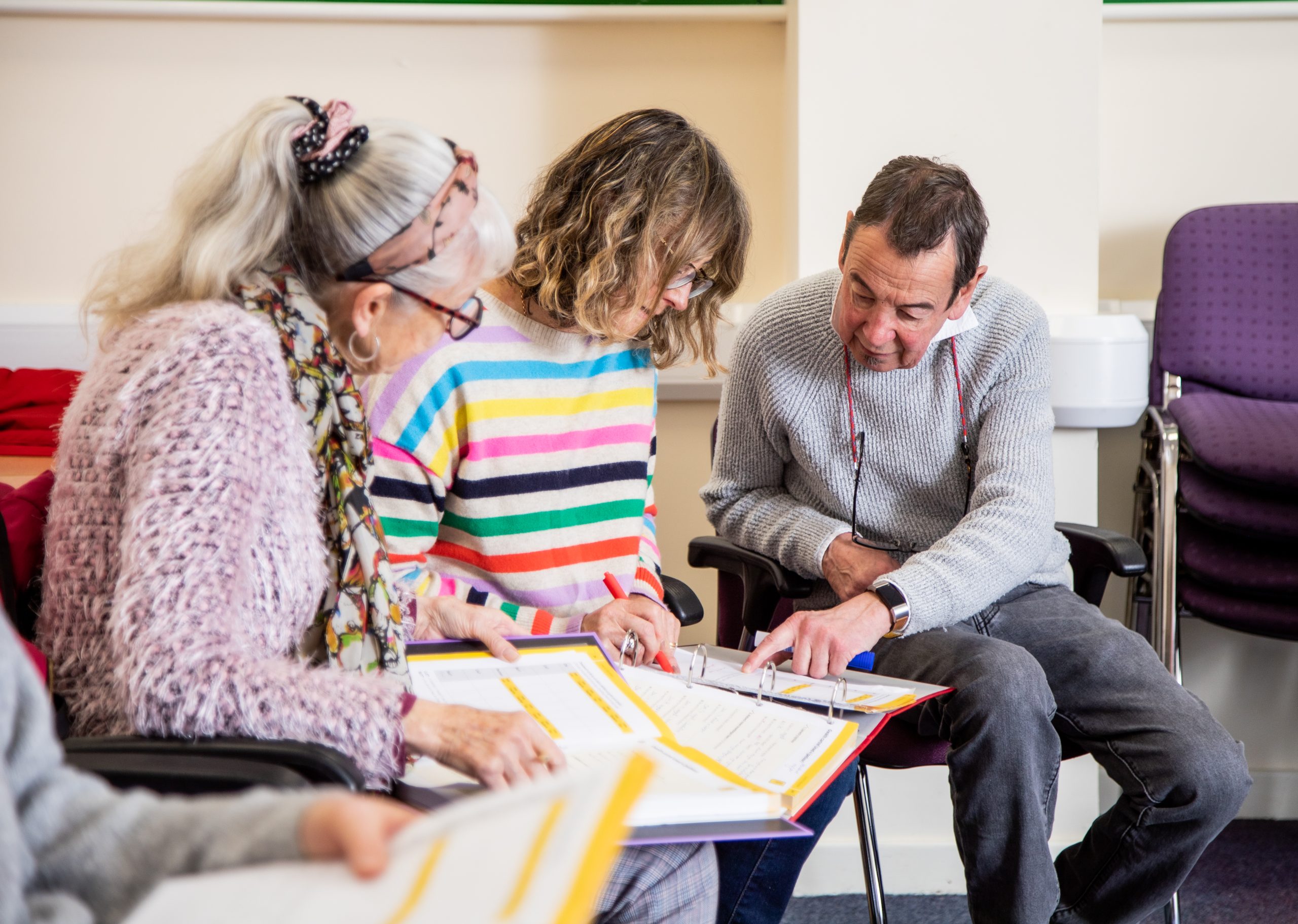 Three adults sitting and reviewing documents in binders together, with one person pointing at a page.