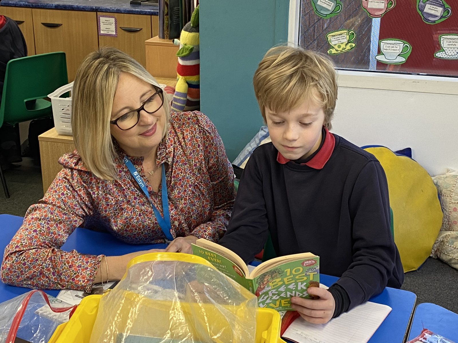 An inspector and a young student read a book together in a classroom setting.