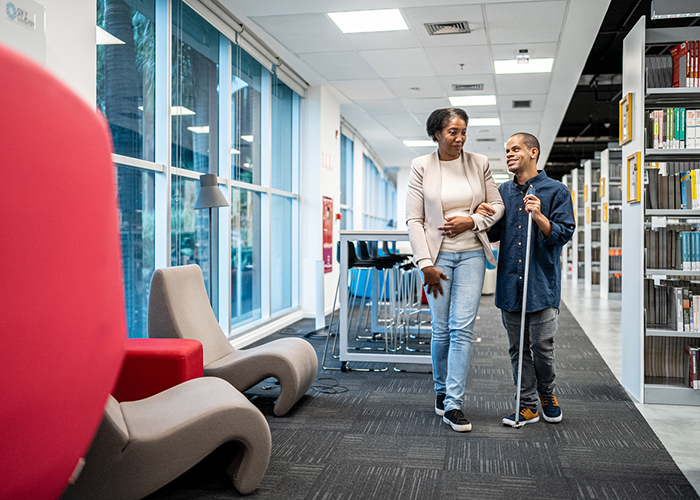 A woman assisting a young person with visual impairment as they walk through a modern library.