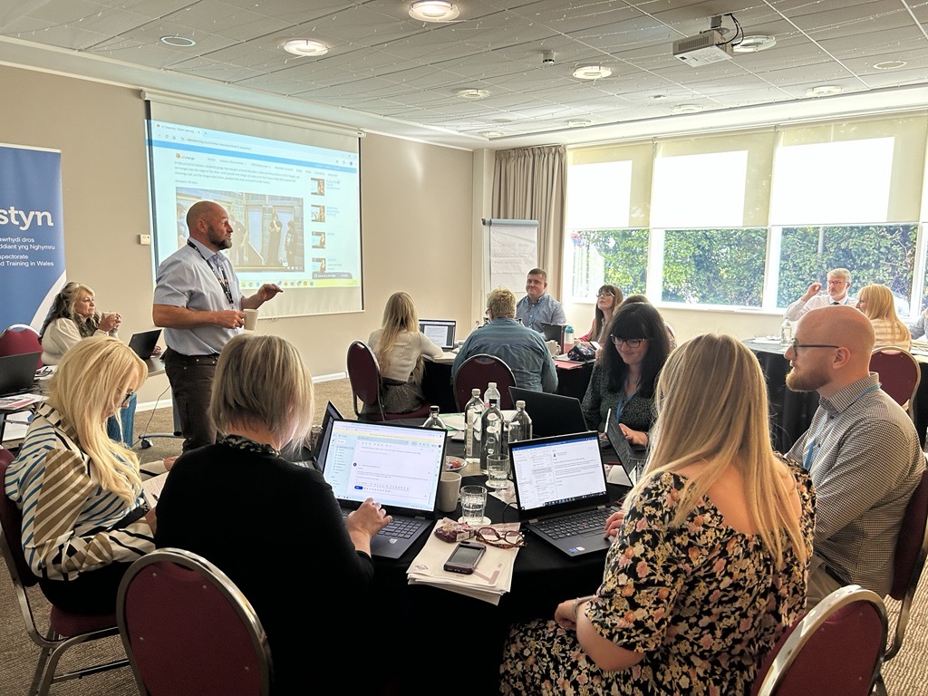 Groups of people sitting around tables listening to a presenter during a training session.