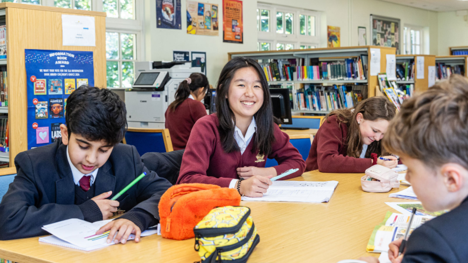 A group of secondary school children working around a desk, with one student smiling at the camera